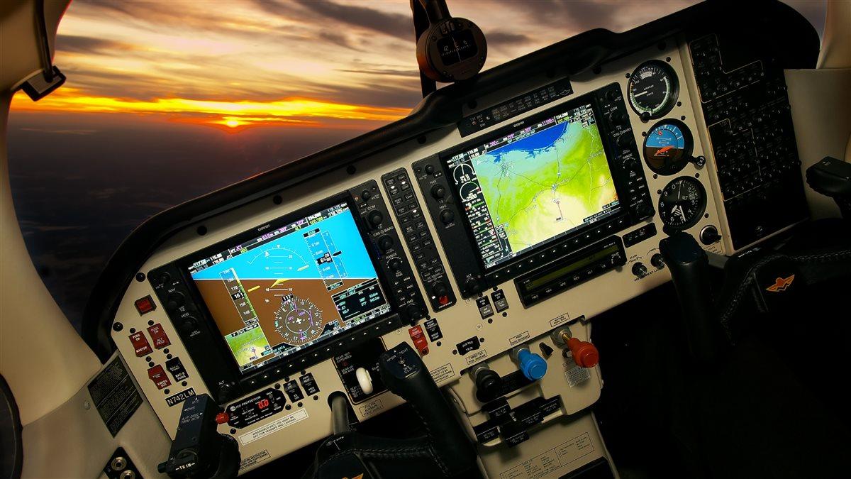 A aeroplane cockpit showing a modern avionics panel, with a sunset outside